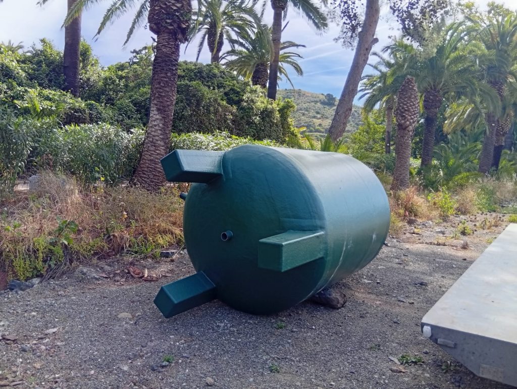 Depósito verde de poliéster con apoyos, tumbado junto a una zona de palmeras antes de su colocación