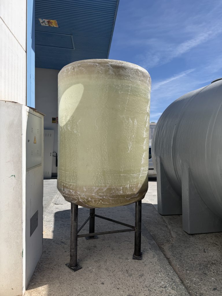 Depósito vertical de poliéster sin acabado opaco sobre una estructura metálica, junto a la fábrica