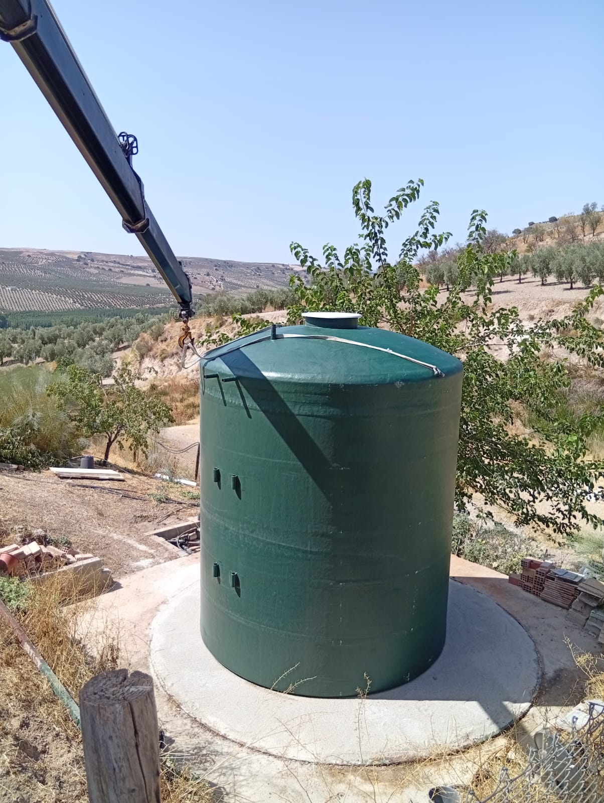 Depósito vertical verde de poliéster durante su descarga sobre una base de hormigón